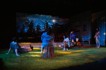 Five people looking at a theatre stage with Christmas trees with starry lights and moon projection. 