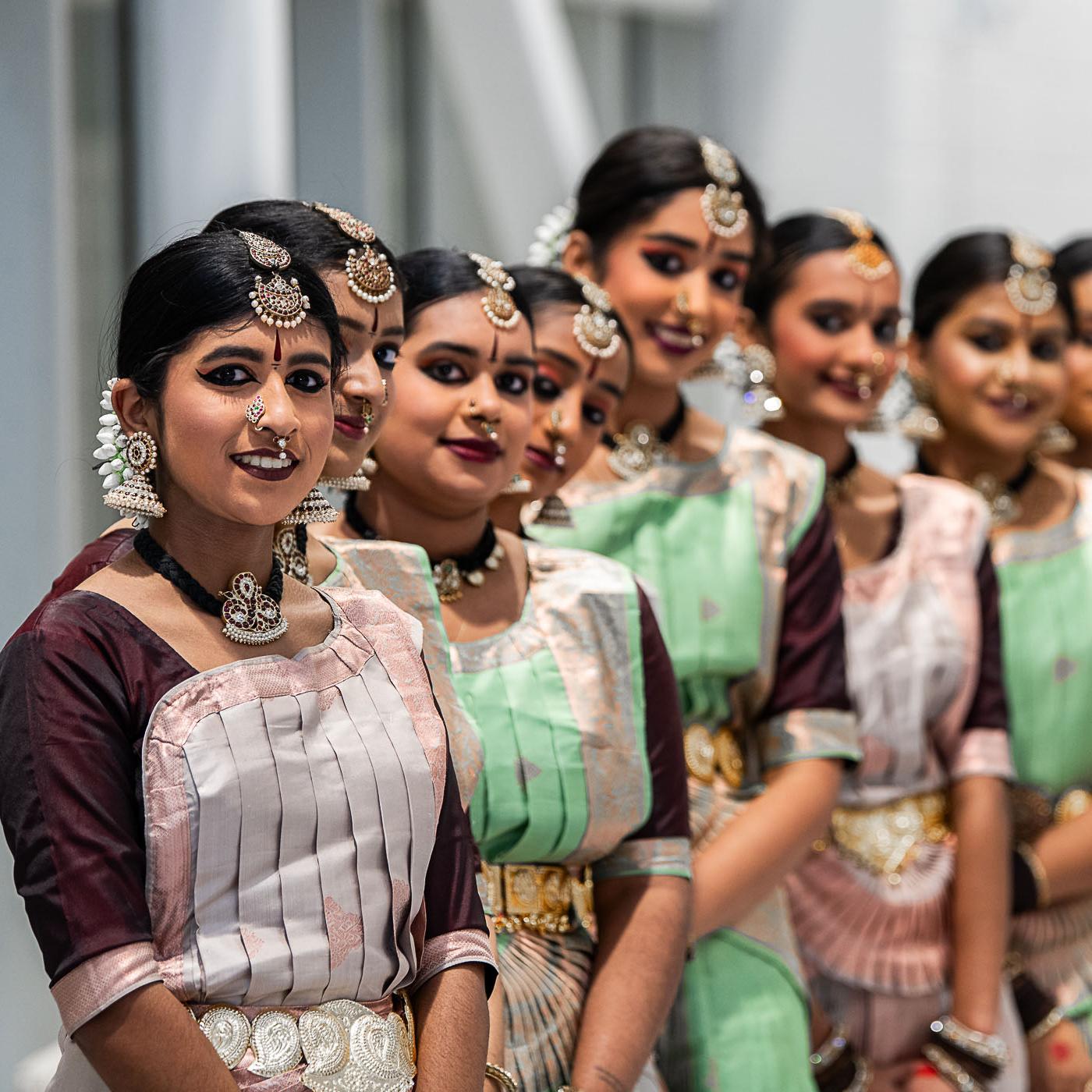 a row of colourfully dressed dancers in traditional outfits, looking at the camera