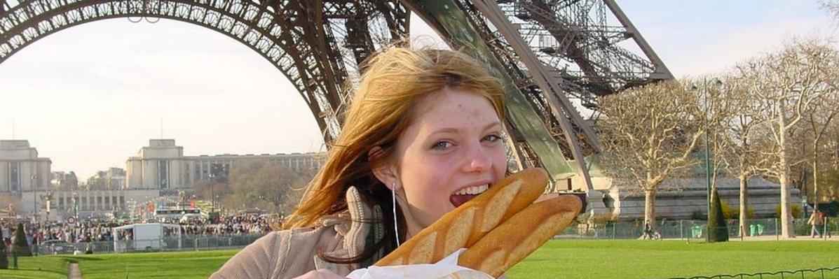 Girl standing in front of the Eiffel Tower eating a baguette
