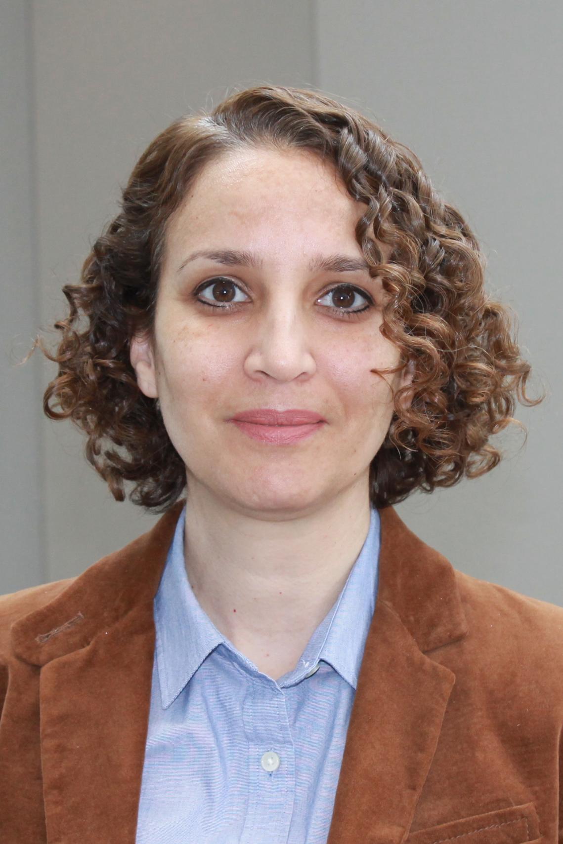 Rania Salem, a woman with curly brown hair and brown eyes wearing a brown blazer and blue shirt