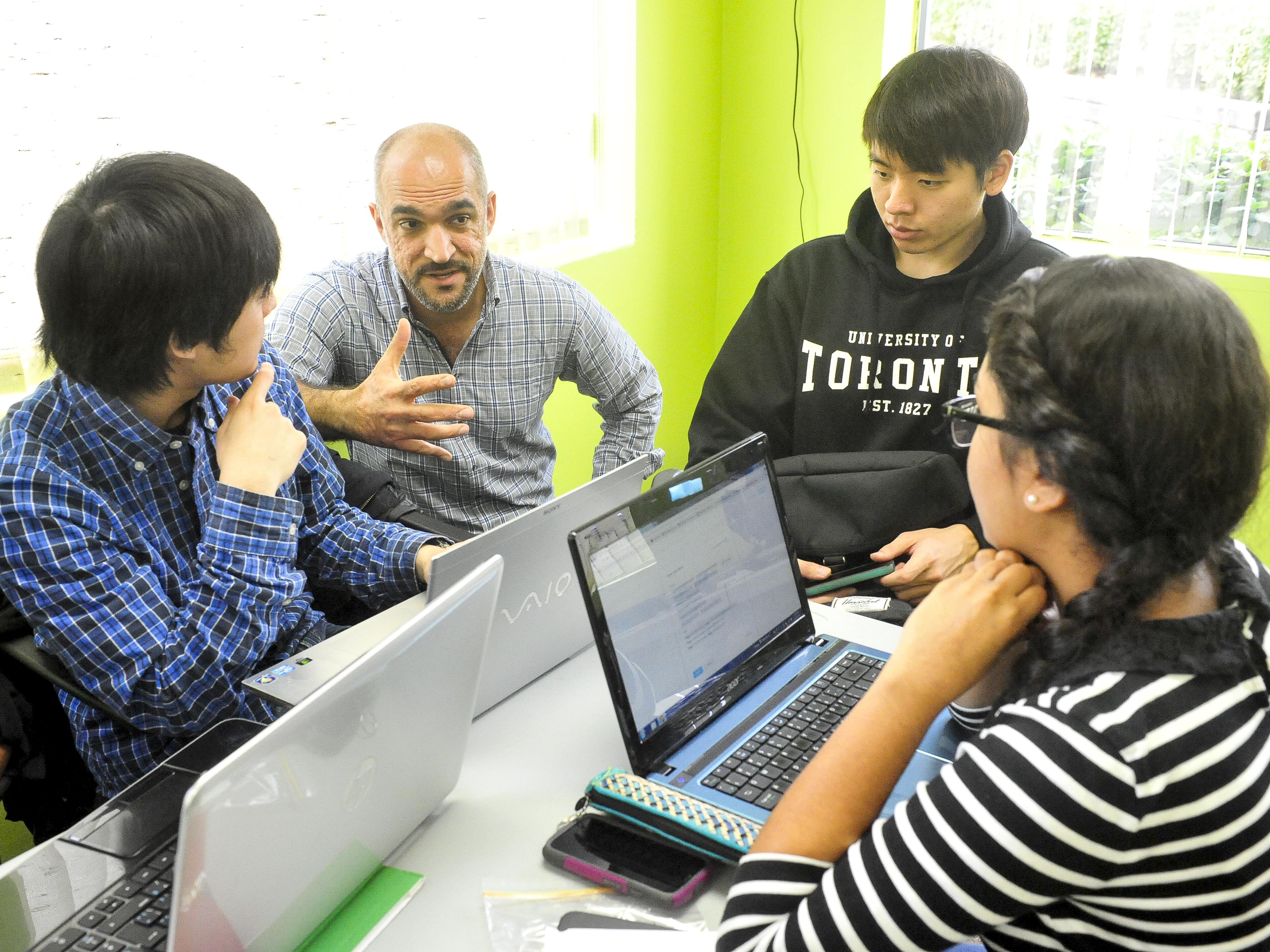 Professor Ahmed Allahwala talking with students working on laptops