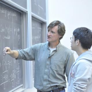 Professor showing student work on a chalkboard