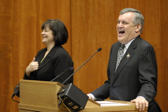 Former Lieutenant Governor David Onley standing at a speaking poduim laughing with a sign language interpreter standing to the side, circa 2009