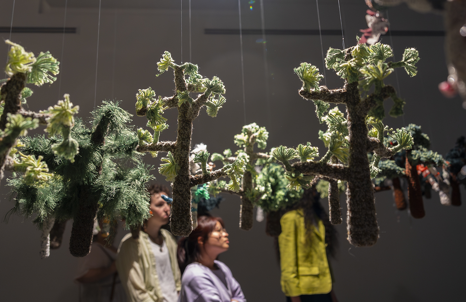 handcrafted figures of trees hung mid air with audience in the background at a gallery