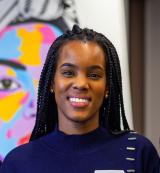 Portrait of Alicia Hall smiling with a colorful painting of a face in the background