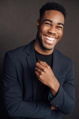 Portrait of Cameron Grant wearing a black shirt and black jacket with a huge smile
