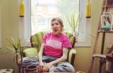 jes sachse sitting on a green chair with a bright pink tshirt in a bright living room with a window in the back