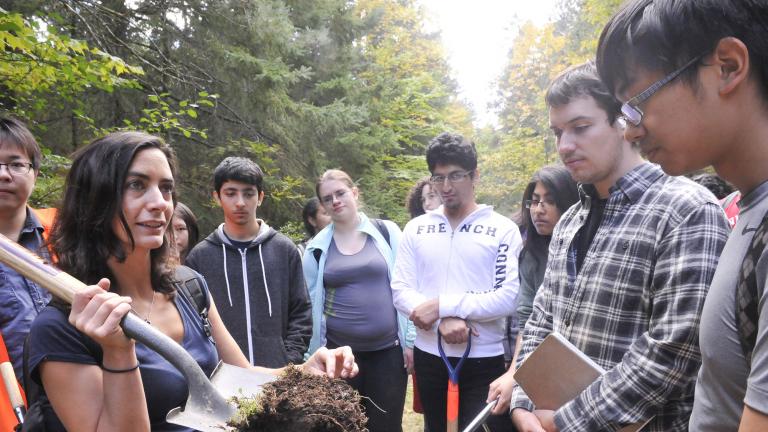 Students on a field trip examining soil on a shovel