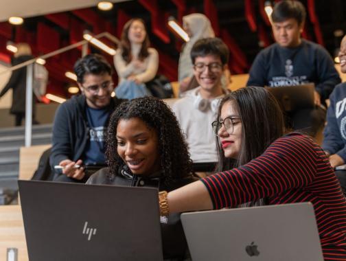 two students in foreground with laptops open and interacting with each other