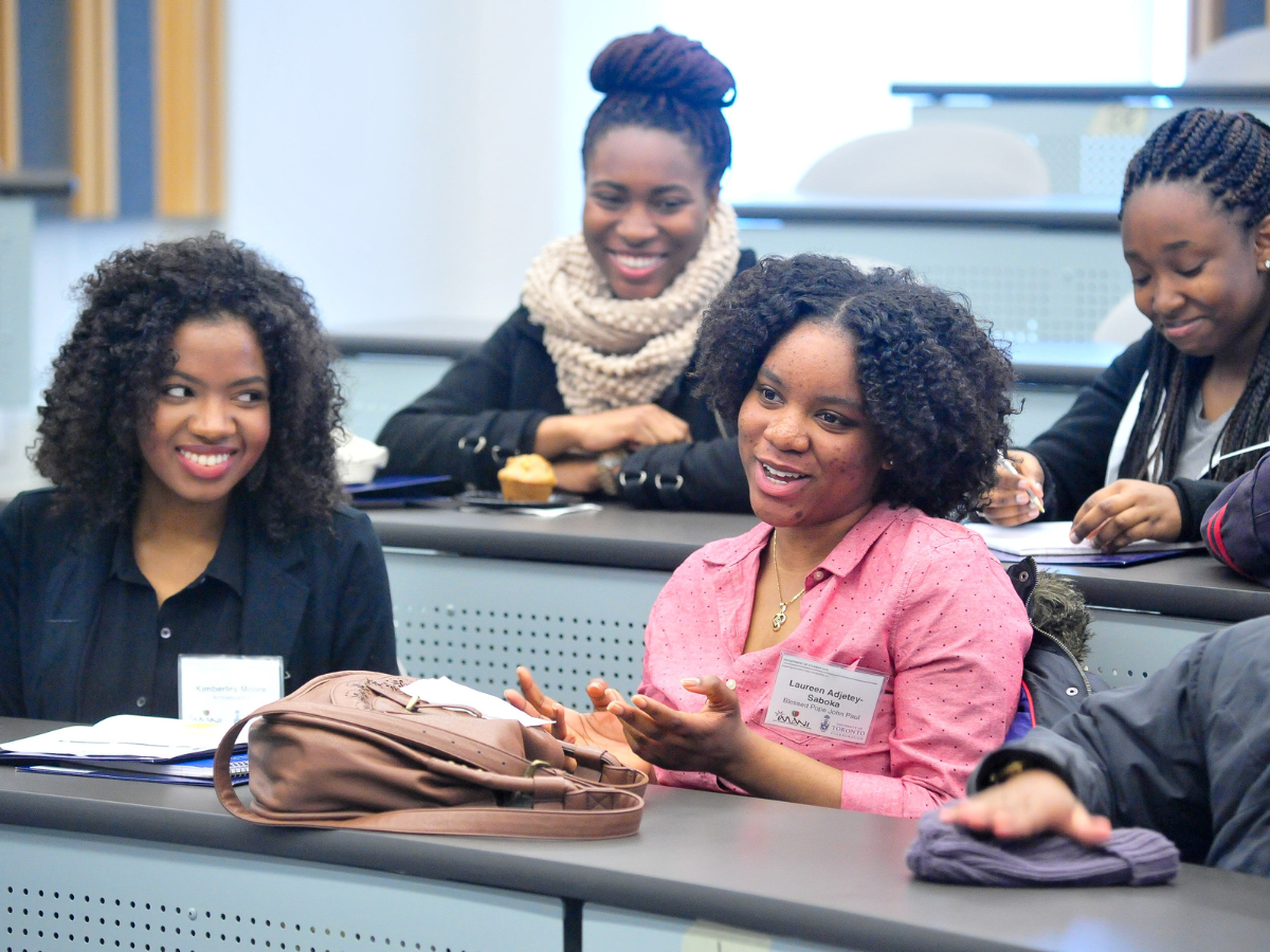 A group of Black female presenting students in class, smiling