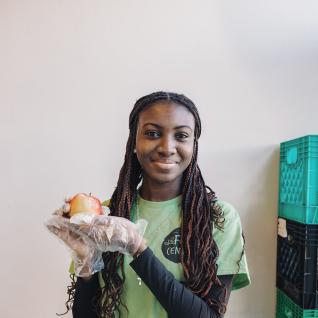 a volunteer in a green SCSU shirt holds up an apple in a plastic gloved hand