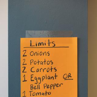an orange sheet taped to a wall saying Limits, 2 onions, 2 potatoes, 2 carrots, 1 eggplant or bell pepper, 1 tomato, 1 apple, head of lettuce