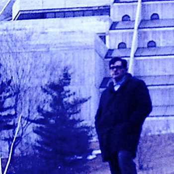 Doug Cockell stands on snowy incline of Valley Land Trail, Bladen building behind him circa 1968