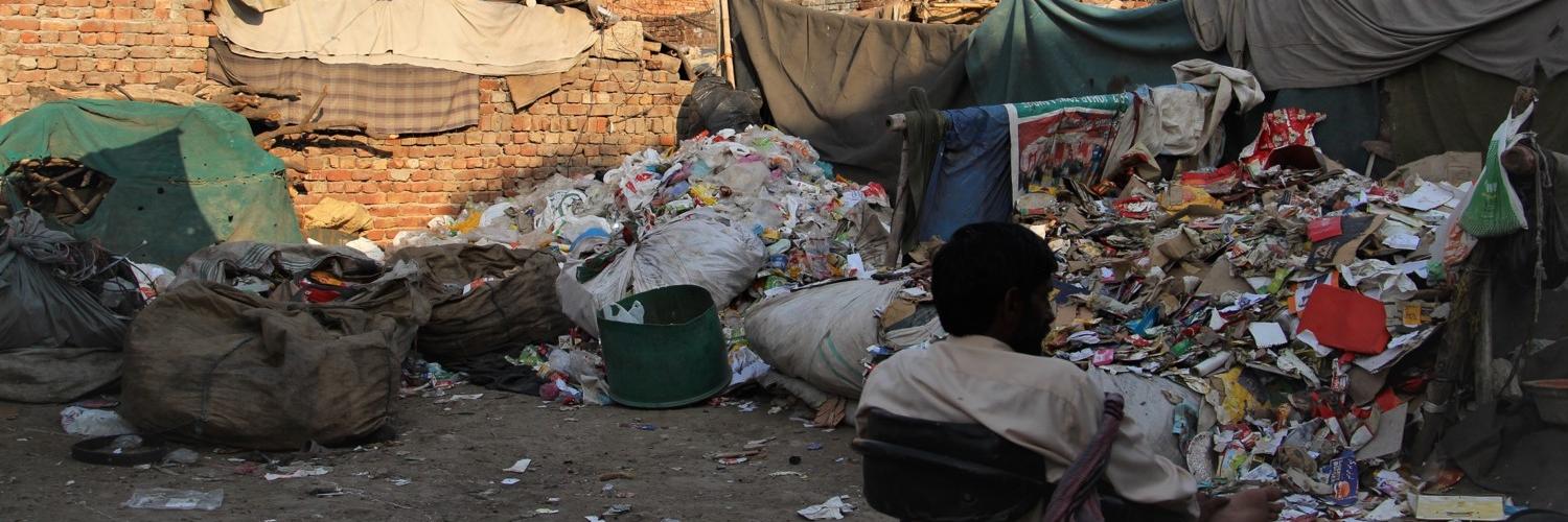 A waste worker in Pakistan sits in a chair beside a pile of refuse