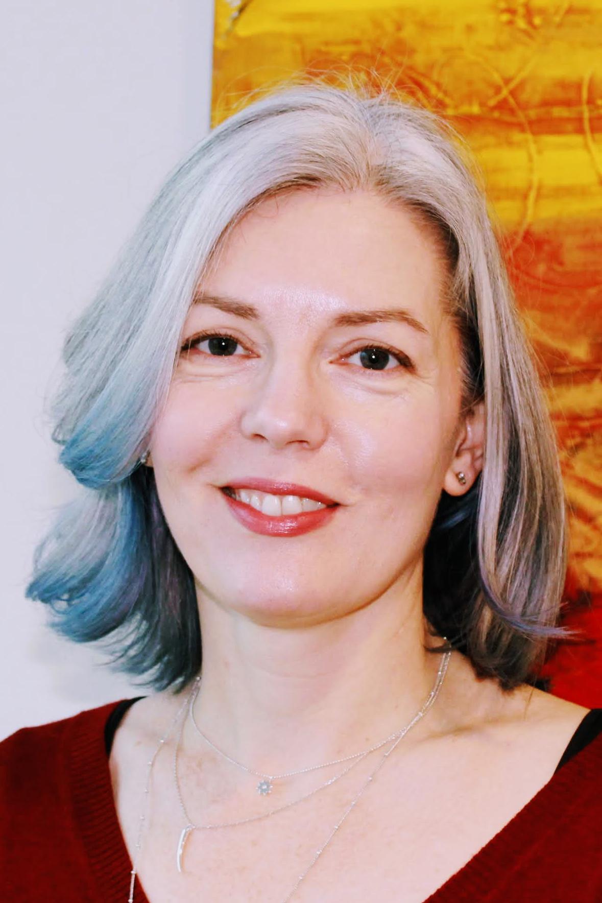 Maggie Cummings, a white woman with white hair, wearing red lipstick and a red shirt.
