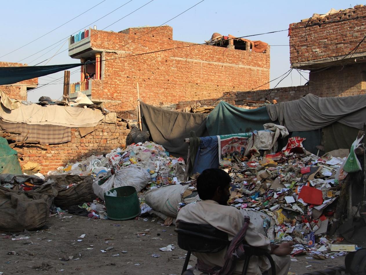 A waste worker in Pakistan sits beside a pile of refuse