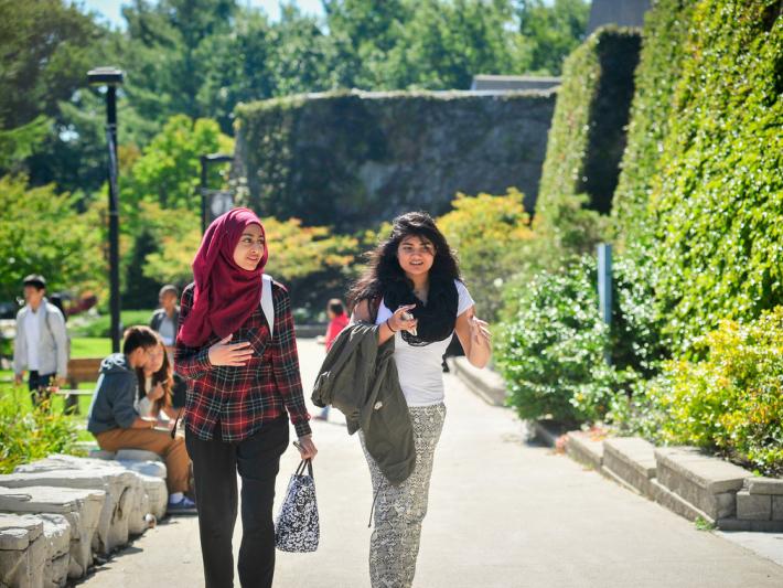 Two women walk and talk outside the H-Wing: Alumni Mentorship Program