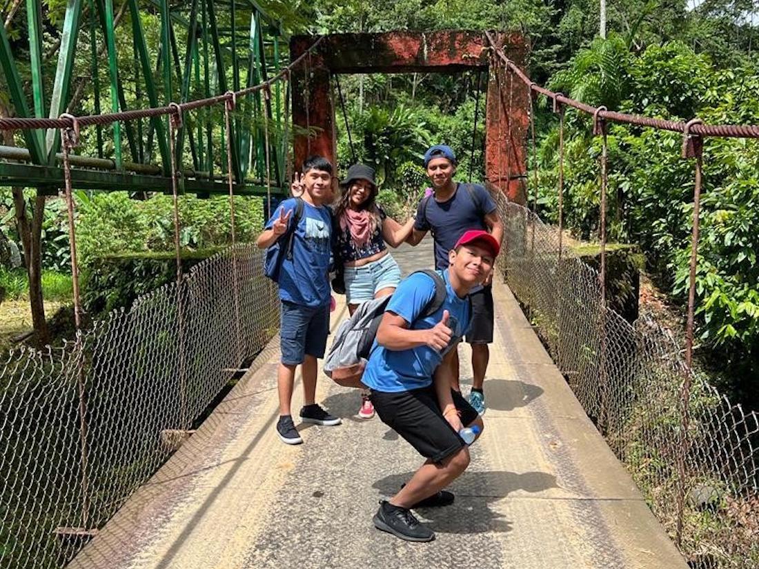 Students on suspension bridge with lush green trees in background