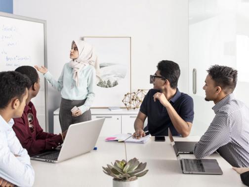 5 students in office space with whiteboard and laptops