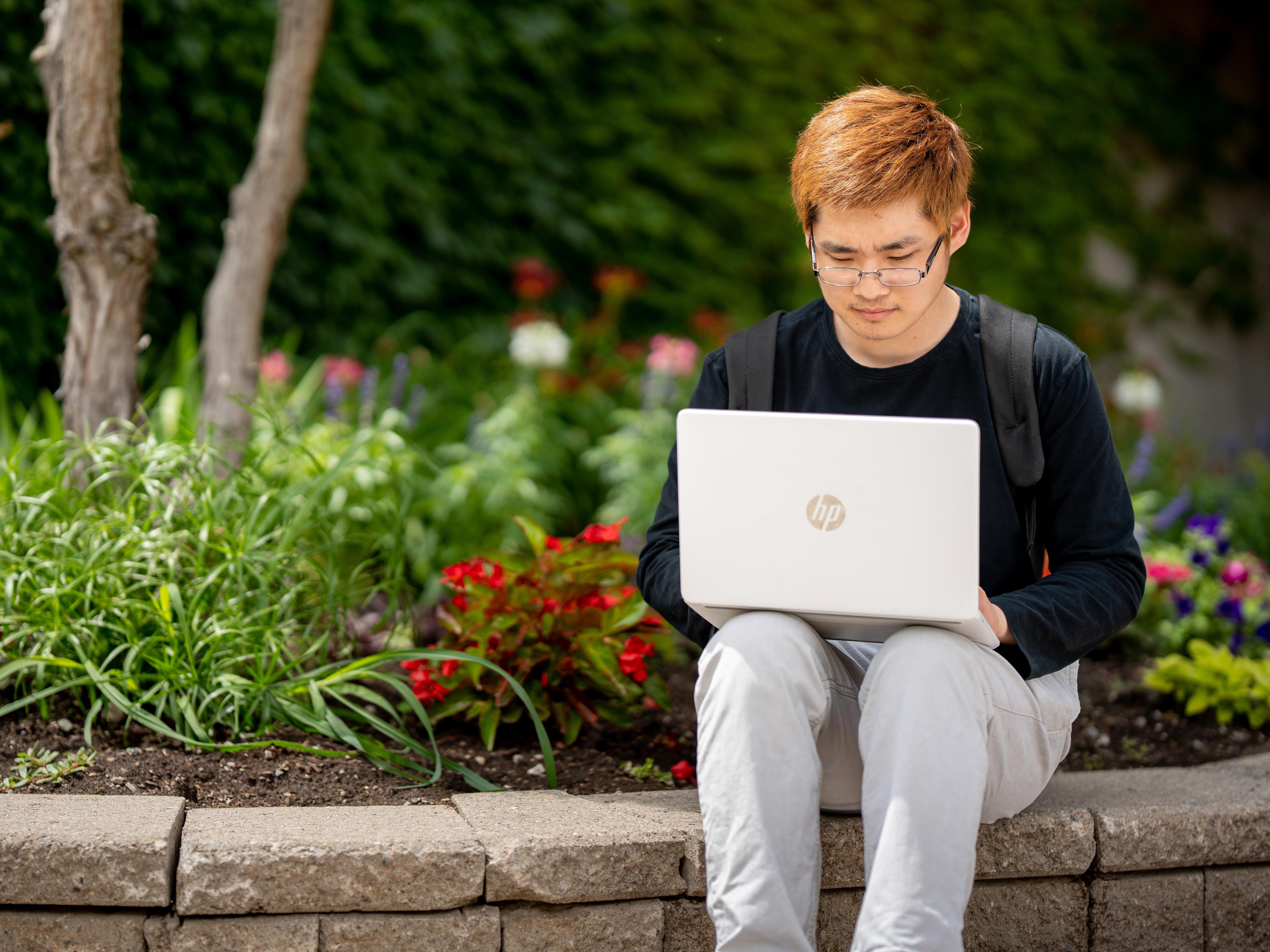 Student sitting with laptop outdoors