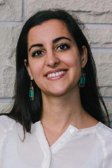 Headshot of Siera in front of brick wall wearing a white shirt and turquoise and metal dangling earrings