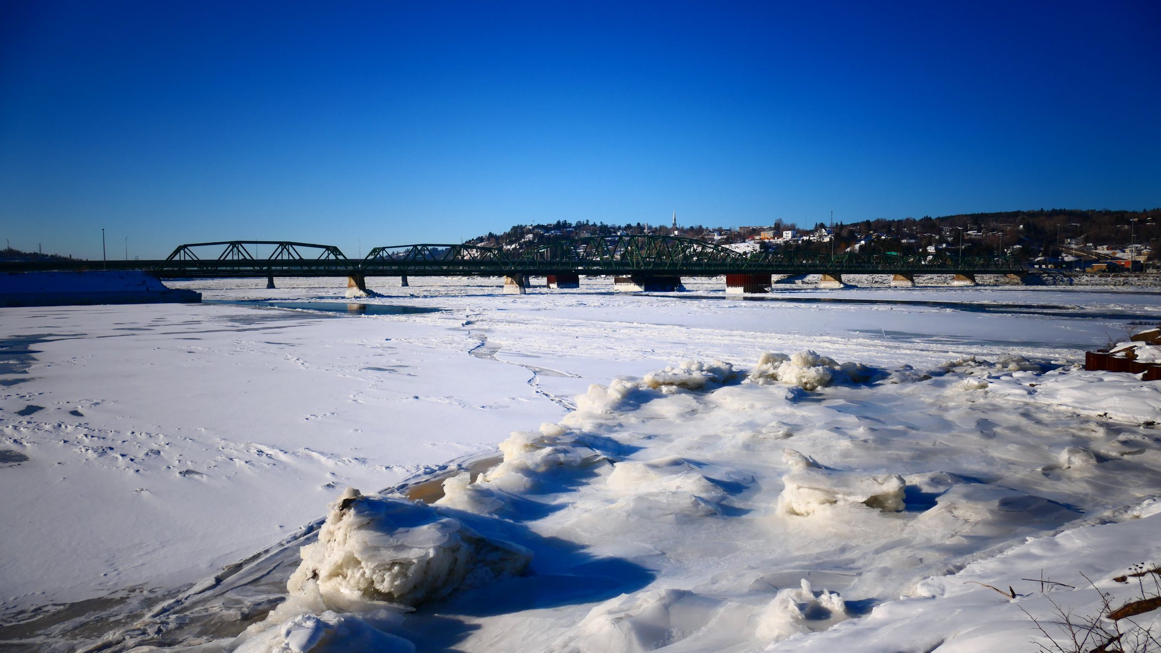 The Sainte-Anne Bridge in Chicoutimi, Saguenay, QC, on a bright winter's day, with the Saguenay river mostly frozen over.