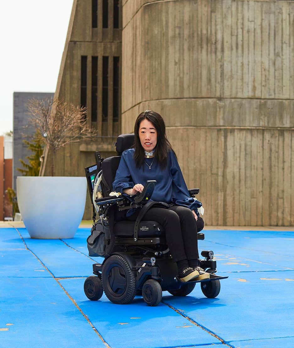 Emily Chan sits in her power wheelchair outdoors on UTSC campus
