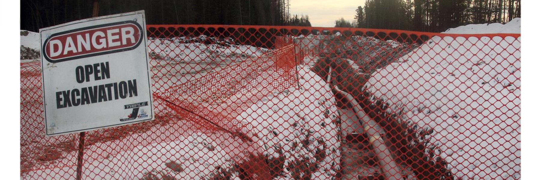orange construction fence with Open Excavation Sign -- snowy forest setting