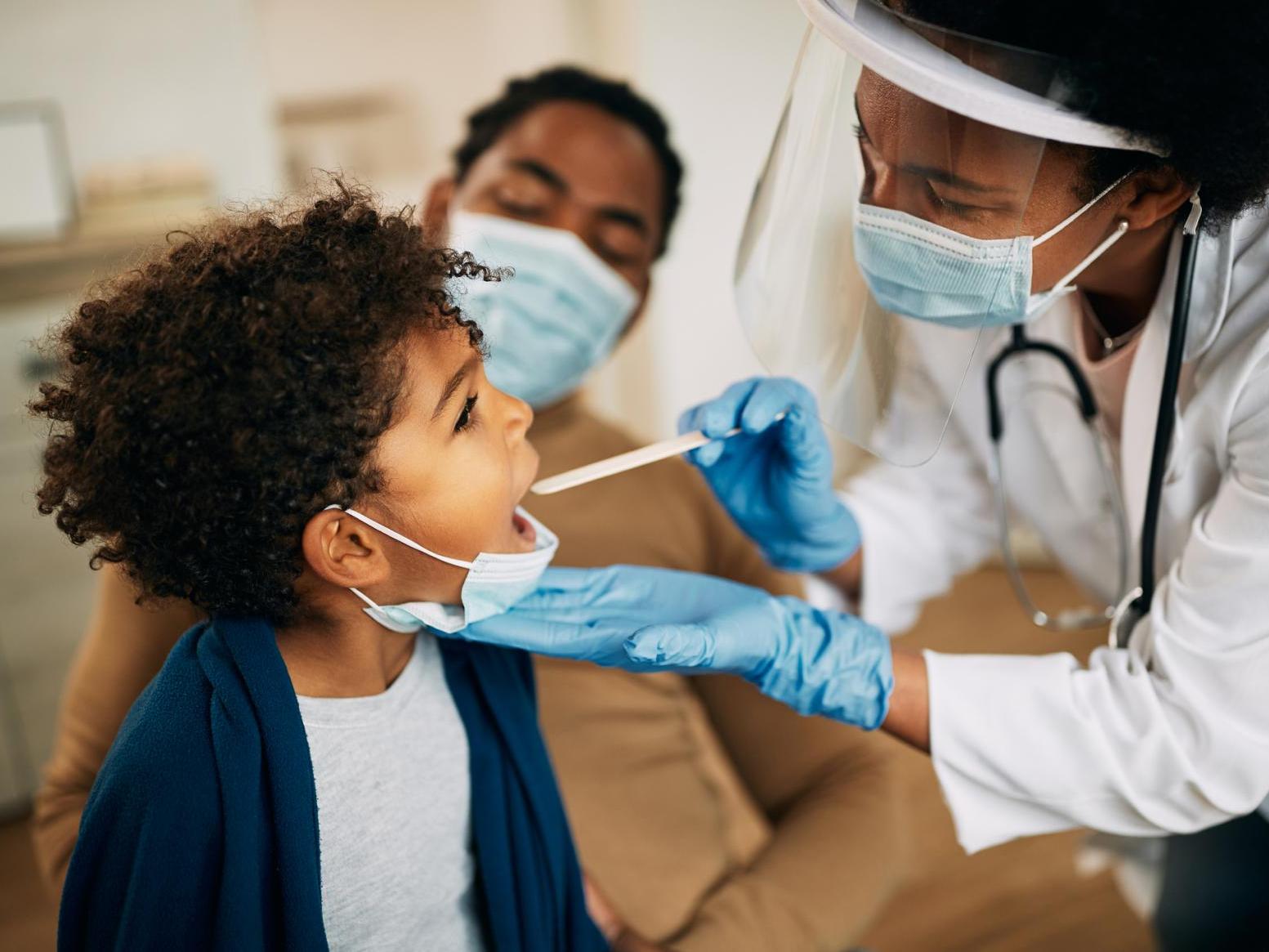 A young Black boy has his temperature taken by a Black female doctor