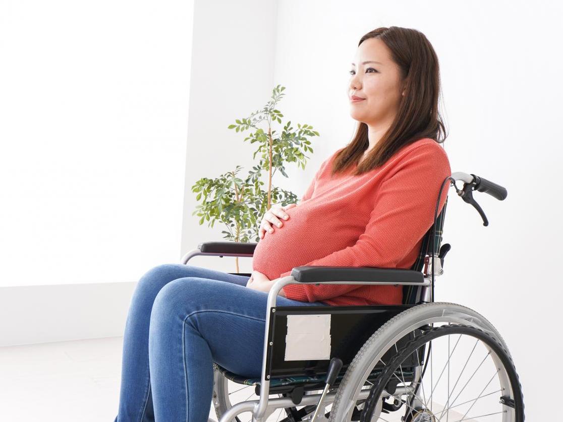 A pregnant woman sits in her wheelchair, with her hand on her belly, smiling