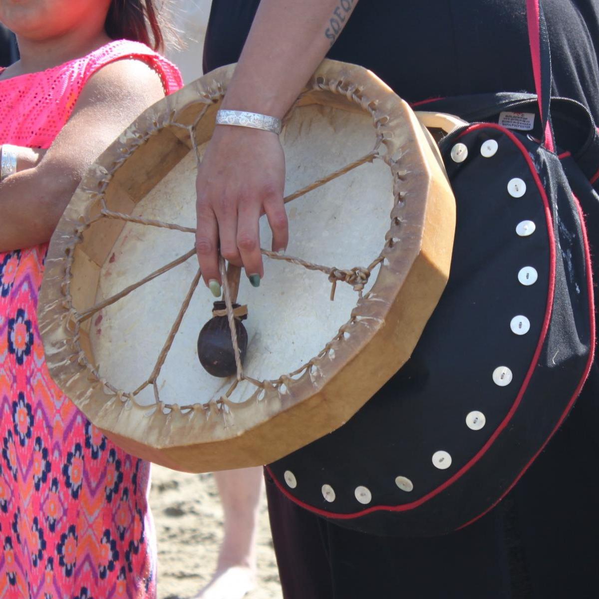 Indigenous woman holding a drum, a young Indigenous girl standing nearby