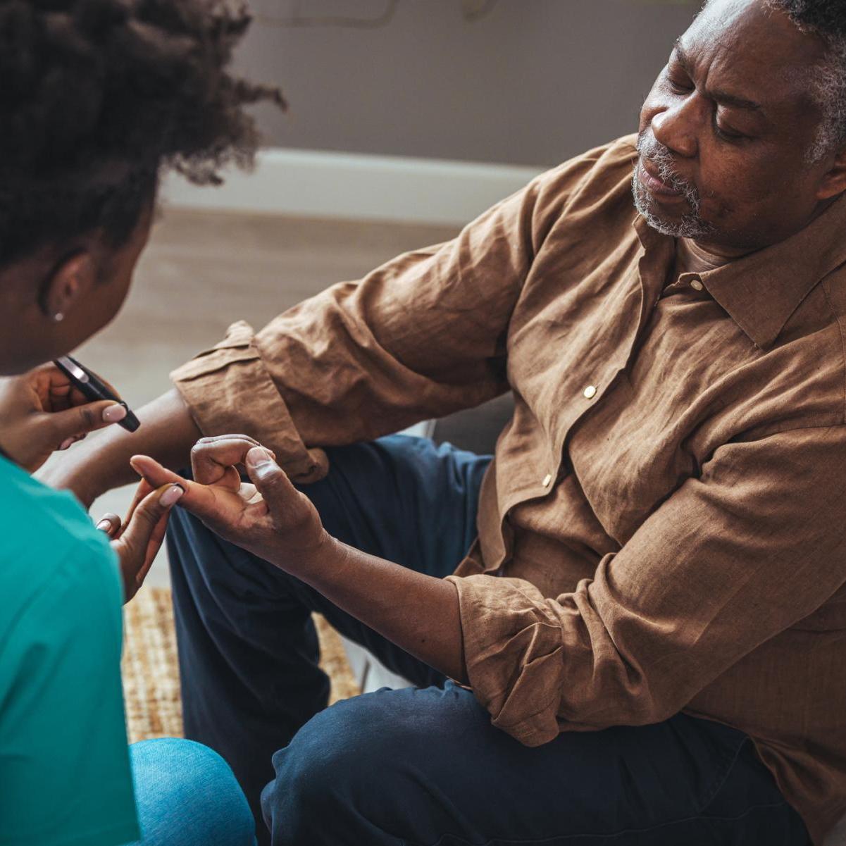 A Black female medical professional tests an older Black man for diabetes
