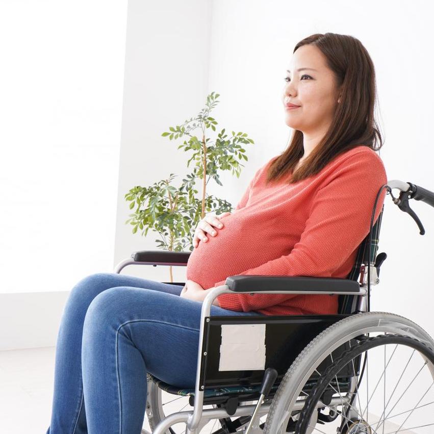 A pregnant woman sits in a wheelchair, rubbing her bump