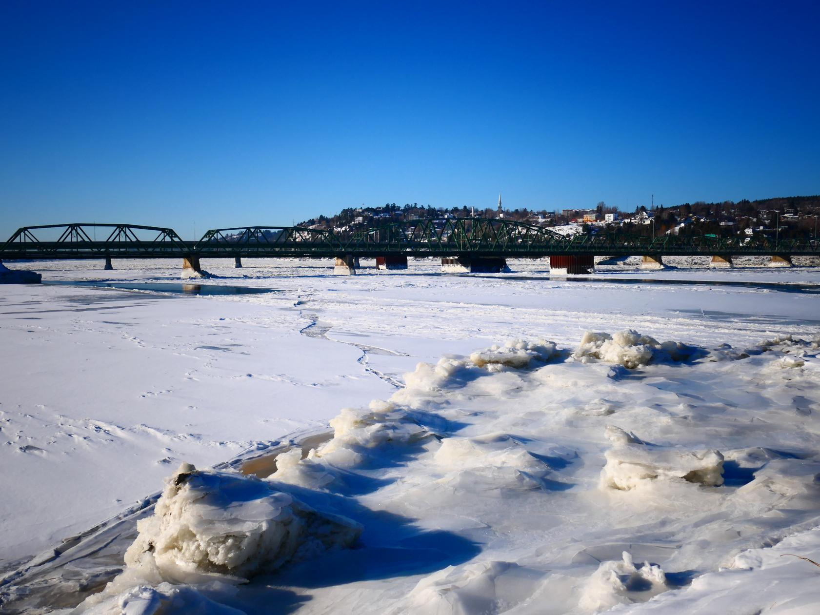 The Sainte-Anne Bridge in Chicoutimi, Saguenay, QC, on a bright winter's day, with the Saguenay river mostly frozen over.