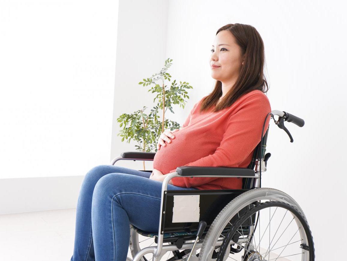 A pregnant woman in a wheelchair rubs her baby bump