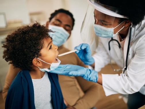 A young Black boy has his temperature taken by a Black female doctor