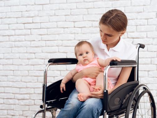 A white woman with blonde hair sits in a wheelchair holding a chubby, healthy baby