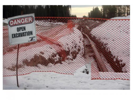 orange construction fence with Open Excavation Sign -- snowy forest setting