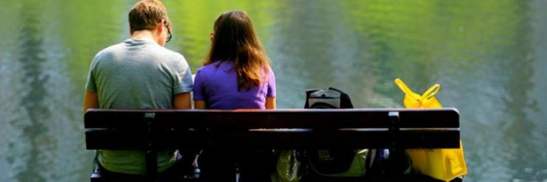two people sitting at a bench by the lake
