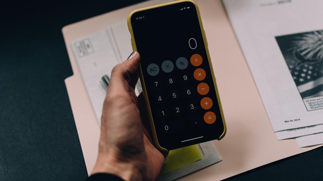 A hand holds a calculator over a folder.