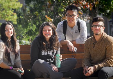 Students sitting on a bench, one behind, looking forward