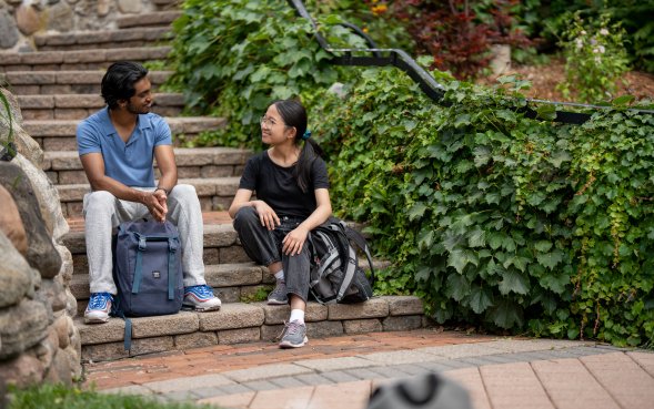 Two students on stone steps next to ivy, in discussion