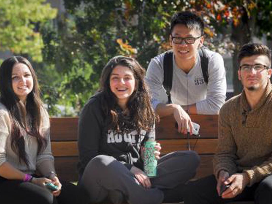students sitting on a bench outside campus