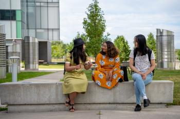 Three students sitting together and chatting outside on campus