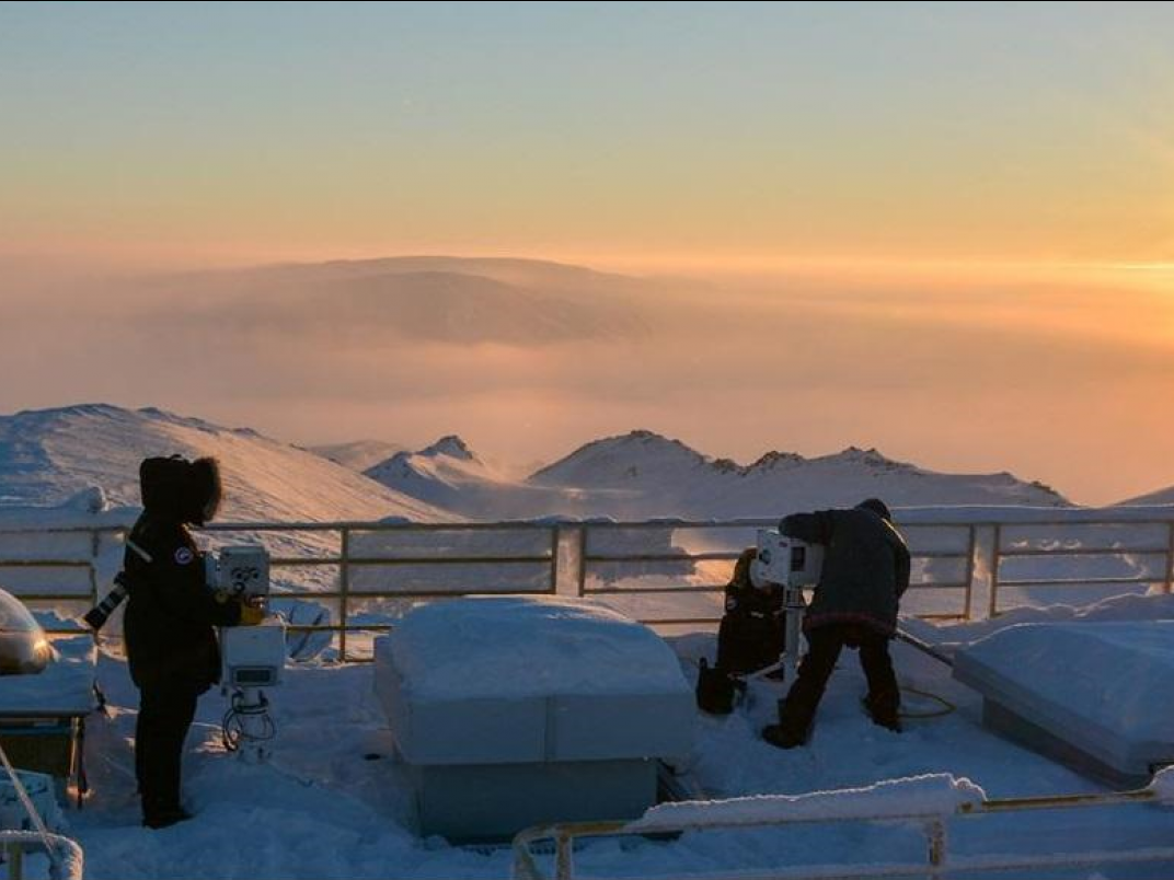 Arctic view of mountains, people in parkas and the sun