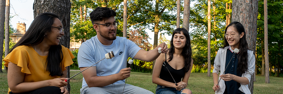 U of T Scarborough Students sitting by campfire roasting marshmallows