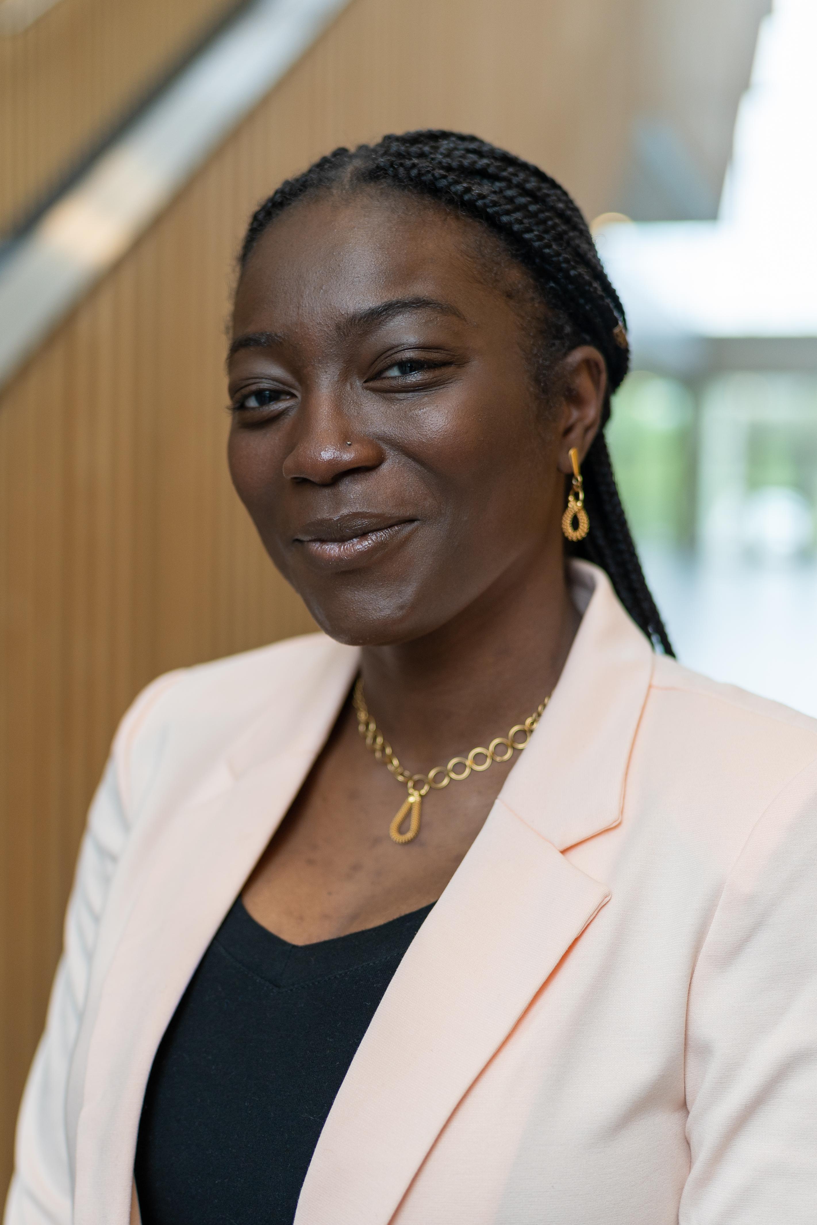 A photo of Efe in Highland Hall, UTSC. She is in a black blouse and a peach-toned blazer.