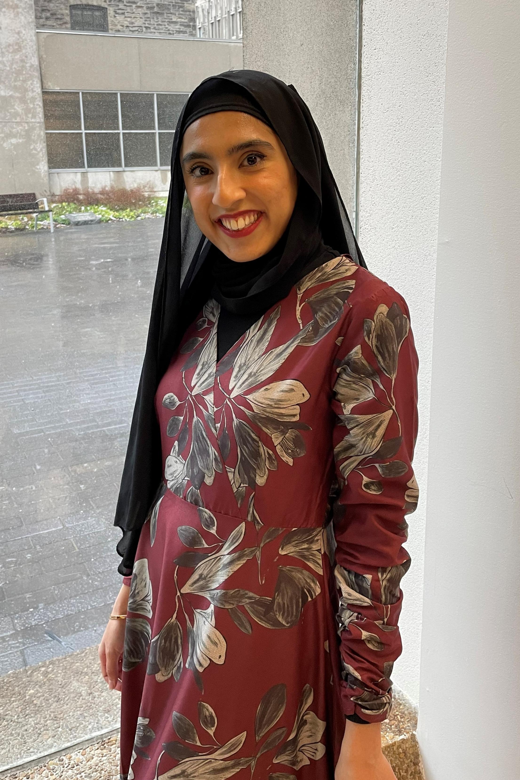 A photo of Laveeza. She is in a red floral dress and black hijab.