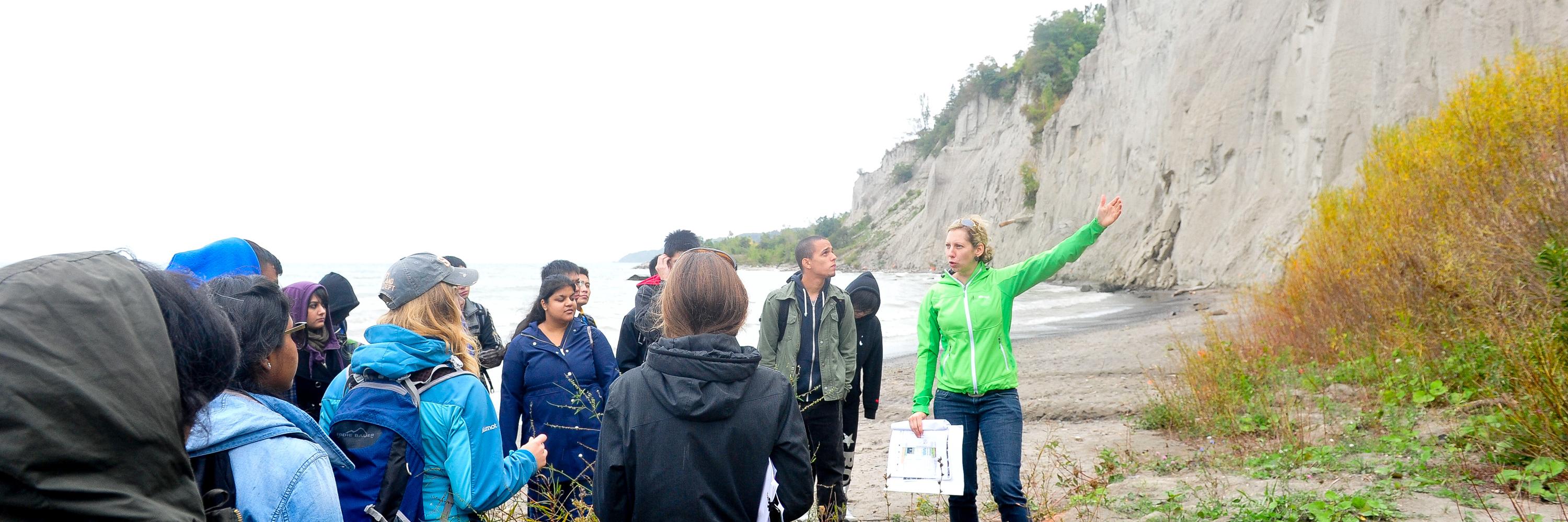 A professor speaks with students on a field trip to the Scarborough Bluffs, seen in the background