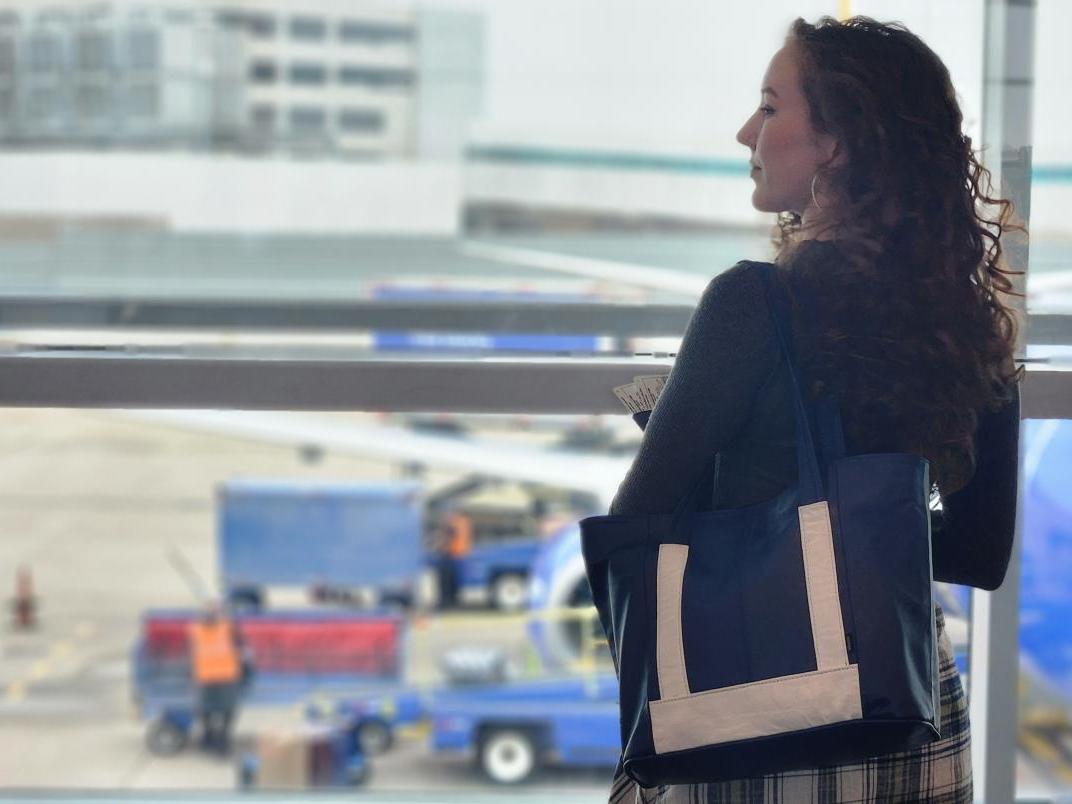 A woman carrying a leather bag in front of a window at an airport